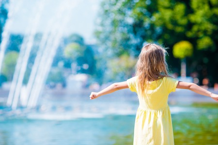 Cute little girl playing near city fountain on hot and sunny summer dayの写真素材