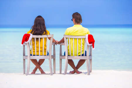 Rear view of young couple in Santa hats relaxing on tropical beach during Christmas vacationの写真素材