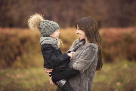 Portrait of cute girl and happy mother in yellow autumn forest on a warm sunny dayの写真素材