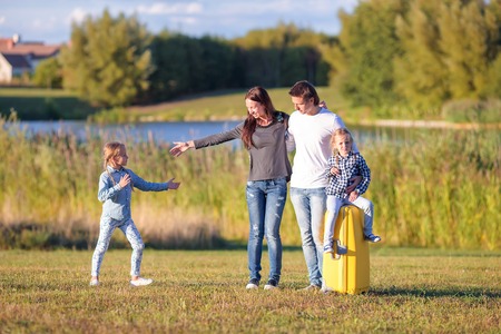 Happy family of four with suitcase walking outdoorsの写真素材