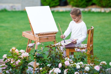 Happy girl painting a picture on an easel on a warm dayの写真素材