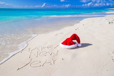 Santa Hat on white sandy beach and Merry Christmas written in the sand