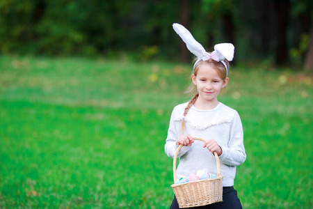 Adorable girl wearing bunny ears holding basket with Easter eggs