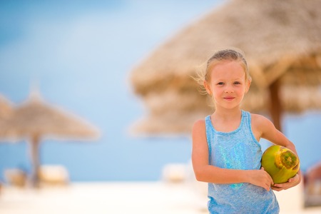 Cute little girl holding coconut cocktail on beachの写真素材