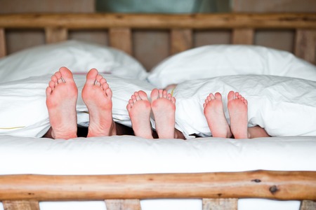 Feet of a family in the bed - father and two kidsの写真素材