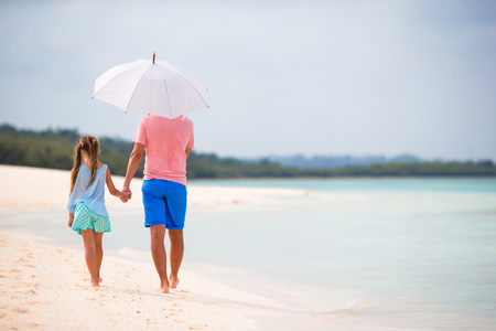 Father and little girl with umbrella hiding from sun at beachの写真素材
