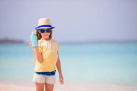 Little adorable girl in swimsuit holds suntan lotion bottleの写真素材