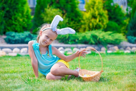 Adorable girl wearing bunny ears holding basket with Easter eggs