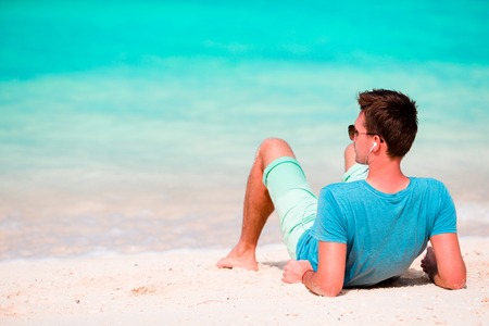 Young beautiful man listening to music on white  beachの写真素材