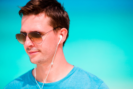 Young beautiful man listening to music on white  beachの写真素材