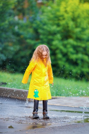 Little girl in raincoat and boots playing in the rain.の写真素材