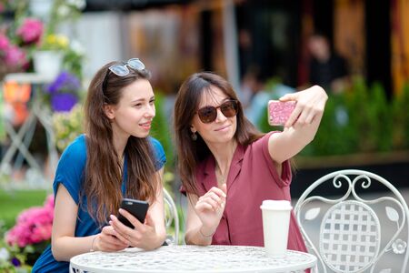 Two nice girl friends sitting in outdoor cafe using smartphoneの写真素材