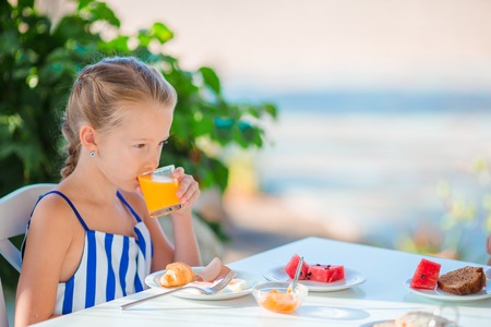 Adorable little girl having breakfast at restaurantの写真素材