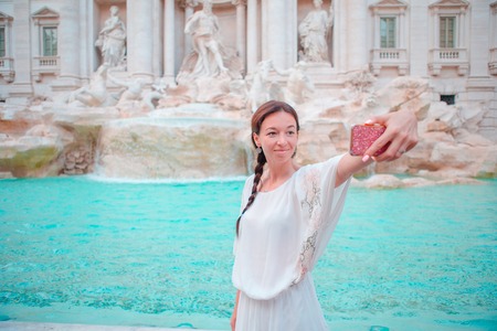 Beautiful girl taking selfie by the Fountain of Trevi in Rome. Happy woman enjoy her european vacation in Italyの写真素材