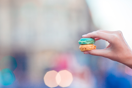 Girl holding colorful French macarons in hands background lively streetの写真素材