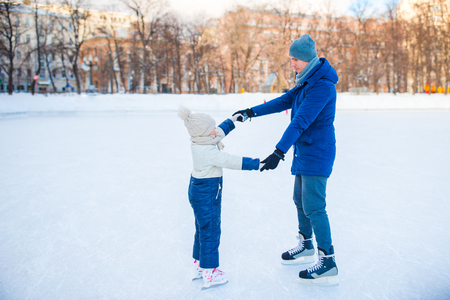 Young father and adorable little girl have fun on skating rink outdoorsの写真素材