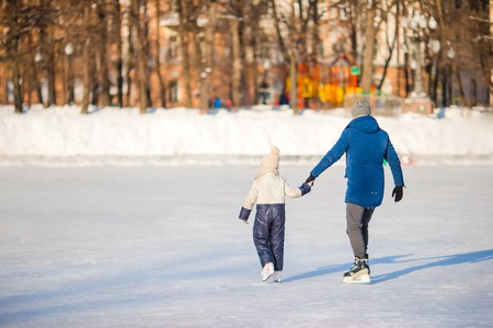 Little adorable girl with father learning to skate on ice-rinkの写真素材