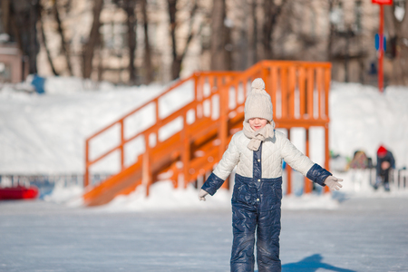 Adorable little girl skating on the ice rink outdoors at warm winter dayの写真素材