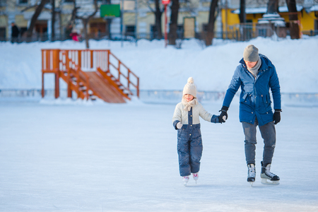 Little adorable girl with father learning to skate on ice-rinkの写真素材