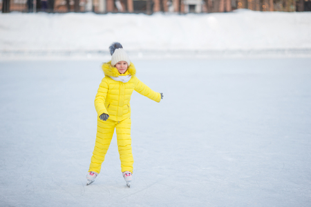 Adorable little girl skating on the ice rink outdoors at warm winter dayの写真素材