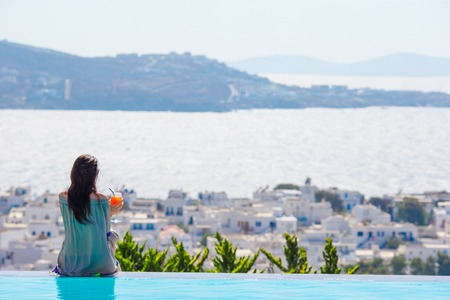 Back view of young woman relaxing on the edge of pool with amazing view on Greeceの写真素材