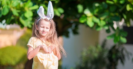 Adorable little girl wearing bunny ears with Easter eggs on spring dayの写真素材
