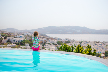 Adorable little girl on the edge of outdoor swimming pool with beautiful viewの写真素材