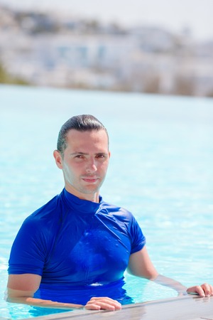 Young happy man relaxing in infinity swimming pool outdoorsの写真素材