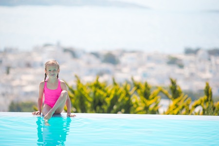Adorable little girl on the edge of outdoor swimming pool with beautiful viewの写真素材
