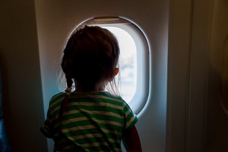 Little girl looking outside of airplane window. Adorable little kid traveling by an aircraftの写真素材