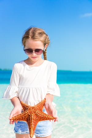 Adorable little girl with starfish on white empty beachの写真素材
