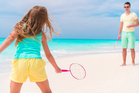 Little girl playing beach tennis on vacation with dadの写真素材