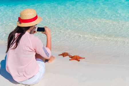 Woman with mobile phone take a photo of red starfish on the tropical beachの写真素材