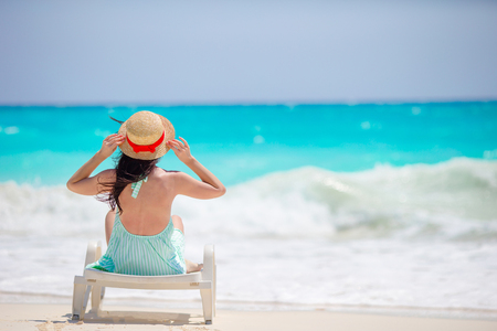 Back view of girl in hat on a tropical beach looking on the beautiful seaの写真素材
