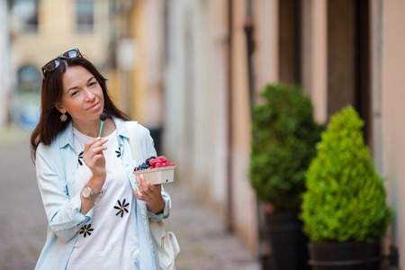 Woman with berries on the old street in the city. Blueberries, raspberries, strawberries, cherries and blackberries in small basket. Gardening, agriculture, harvest and forest concept.の写真素材
