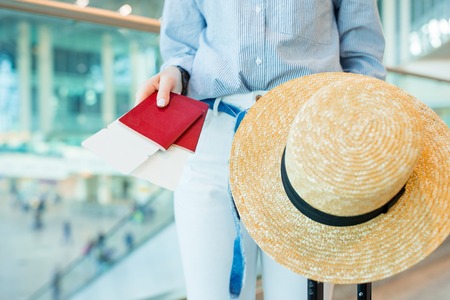 Close-up of passports with boarding pass in female hands. Young woman ready to travel with baggage and straw hatの写真素材
