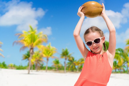 Little happy girl with big coconut on the beach in the palm groveの写真素材