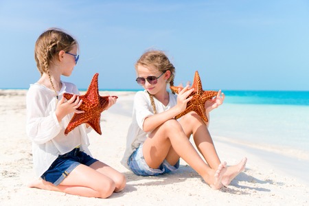 Adorable little girls with starfishes on white empty beachの写真素材