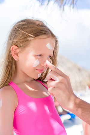 Father applying sun cream to daughter nose. Portrait of cute girl in suncreamの写真素材