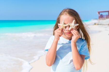 Adorable little girl with starfish on white empty beachの写真素材