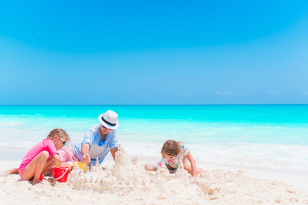 Father and little daughters making sand castle at tropical beachの写真素材