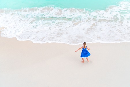 Adorable little girl dancing on white tropical beach. View from above of a deserted beach with turquoise waterの写真素材