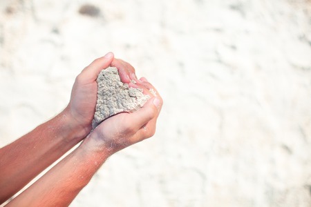Closeup male hands holding white tropical beach form heart shape background the seaの写真素材