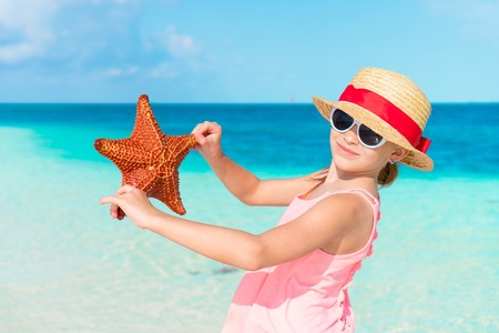 Adorable little girl with starfish on white empty beachの写真素材