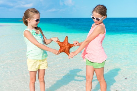 Adorable little girls having fun on the beach full of starfish on the sandの写真素材