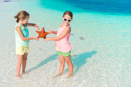 Adorable little girls having fun on the beach full of starfish on the sandの写真素材