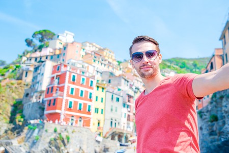 Young man taking selfie with beautiful view at old italian village Riomaggiore, Cinque Terre, Liguria, Italy. European italian vacation.の写真素材