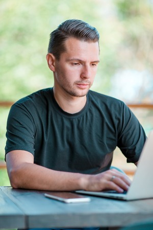 Young man with laptop in outdoor cafe drinking coffee. Man using mobile smartphone.の写真素材