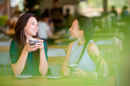 Happy smiling young women with coffee cups at cafe. Communication and friendship conceptの写真素材
