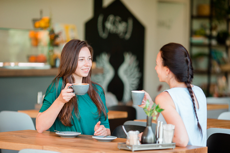 Happy smiling young women with coffee cups at cafe. Communication and friendship conceptの写真素材